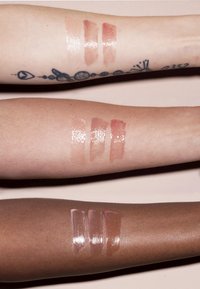 Tre braccia mostrano delle strisce di prodotto labbra: tonalità chiare, medie e scure. Le sfumature vanno dal nude al rosa, con finiture lucide.