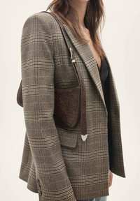 Bruine lederen schoudertas met gegraveerd bloemmotief, gecombineerd met een geruite blazer met structuur. Bevestiging met haak en verstelbare riem.