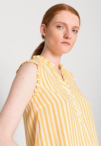 Blusa sem mangas amarelo e branca com riscas, com decote franzido, fecho de botão e um corte descontraído para conforto e estilo.