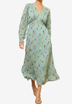 Femme portant une robe midi bleu clair avec des pois multicolores brillants et des manches longues bouffantes, associée à des talons dorés à brides.