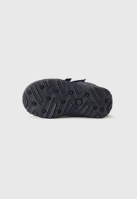 Černá gumová podrážka dětské boty s kruhovými a liniovými vzory na jednobílém pozadí.