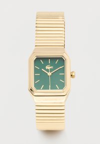 Ρολόι χειρός σε χρυσό τόνο με πράσινο τετράγωνο καντράν, χρυσούς δείκτες ώρας, δείκτες, λογότυπο κροκόδειλου και ραβδωτό μεταλλικό επεκτεινόμενο λουρί.