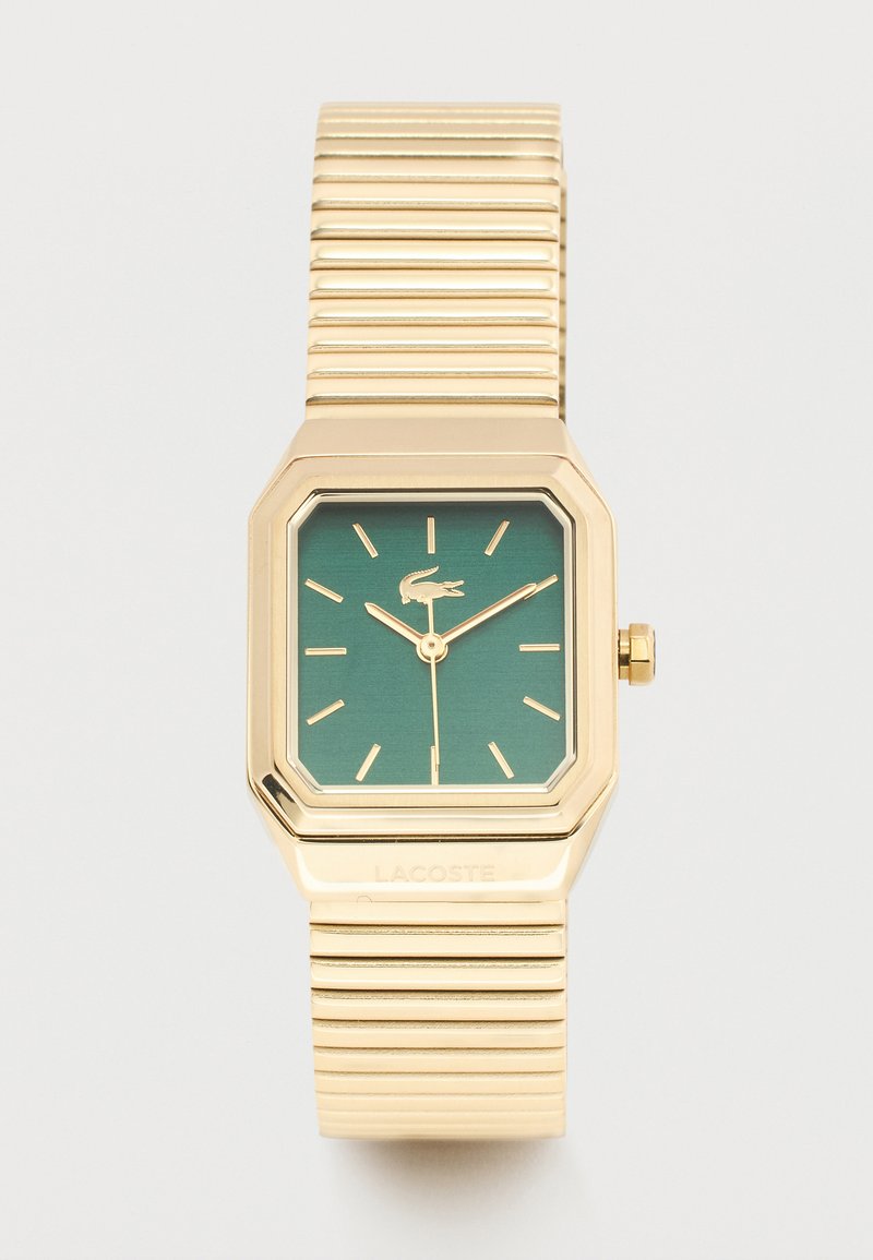 Ρολόι χειρός σε χρυσό τόνο με πράσινο τετράγωνο καντράν, χρυσούς δείκτες ώρας, δείκτες, λογότυπο κροκόδειλου και ραβδωτό μεταλλικό επεκτεινόμενο λουρί.