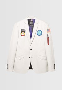 Light gray blazer featuring multiple patches, dark buttons, two front flap pockets, and a zippered red accent on the left sleeve.