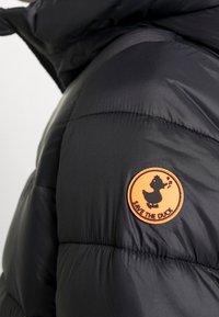 Sort pufferjakke med en orange cirkulær plet, der viser en silhuet af en syngende and og teksten "SAVE THE DUCK" på ærmet.