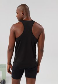 Top desportivo preto sem mangas com um design de costas em "racerback", feito de um tecido suave. Apresenta riscas refletoras nas laterais e um corte ajustado.