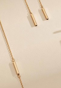Boucles d'oreilles en chaîne de couleur dorée avec des pendentifs rectangulaires, présentant une surface lisse et polie. Conçues avec une apparence simple et elegante.