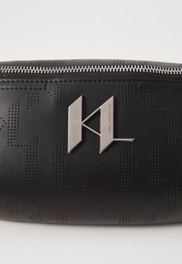 Sorte læderpung med struktureret mønster, sølvfarvet lynlås og en iøjnefaldende metal_logo aksent på fronten.