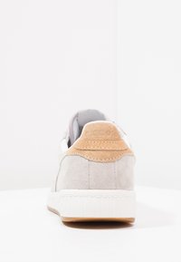 Jasnoszary sneaker zamszowy, z białą gumową podeszwą i jasnobrązowym zamszowym akcentem na pięcie z wytłoczonym logo.