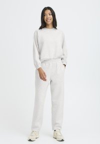 Svetlo šedá mikina s dlhými rukávmi a rebrovanými manžetami, doplnená o zodpovedajúce tepláky s elastickým pásom a bočnými vreckami.