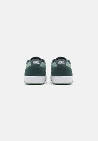 Green suede sneakers with mesh accents, white rubber sole, and Vans logo on the heel and tongue. Rear view shows padded collar and reinforced structure.