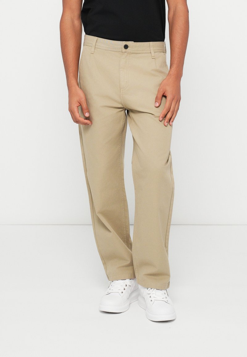 Smėlio spalvos medvilniniai kelnės, tiesaus kirpimo, su šoninėmis kišenėmis ir priekiniais mygtukais. Derinamos su baltais sportbačiais.