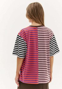 Pasiasta, oversize t-shirt w odcieniach fioletu, pomarańczu, różu i czerni. Krótkie rękawy i okrągły dekolt. Miękka tekstura.