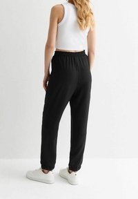 Schwarze Jogginghosen mit elastischem Bund und Bündchen an den Säumen, kombiniert mit einem weißen Crop-Top. Glatte Stofftextur, minimalistisches Design und weiße Sneaker.