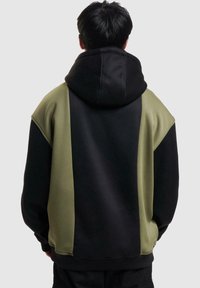 Huvtröja med svart tyg och olivgröna sidopaneler. Strukturerat material, avslappnad passform och ribbade mudd.