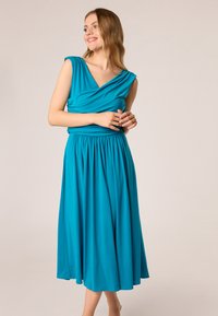 Tyrkysové šaty so priliehavým korzetom, zavinutým výstrihom a krátkymi rukávmi. Plynulá, stredne dlhá sukňa s elastickým pásom. Mäkko hladký materiál.