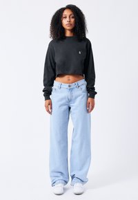Black cropped sweatshirt with a small logo, paired with light blue wide-leg jeans, and white sneakers. Smooth fabric, loose fit, relaxed style.