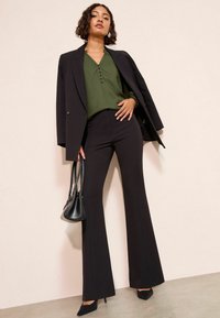 Fekete szabott öltöny, harangszárú nadrággal, sötétzöld blúzzal párosítva, amely gombokkal és fodros ujjal rendelkezik. Tartalmaz egy kis fekete retikült.