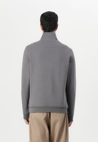 Felpa grigia con colletto alto, maniche lunghe e orlo a coste. Tessuto morbido e design minimalista.
