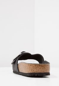 Sandal de cuero negro con plantilla de corcho y suela de goma negra texturizada. Presenta una correa ancha con un hebilla de metal y un diseño de punta abierta.