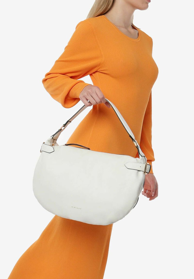 Bolso de hombro de cuero blanco con herrajes plateados, forma curvada y correa ajustable, sostenido por una persona que lleva un vestido naranja acanalado.