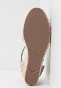 Semelle de sandale compensée beige avec semelle extérieure en caoutchouc texturé et plateforme en paille tissée, présentée en angle sur un fond blanc d'angle.