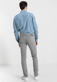 Pantalones gris slim-fit con un diseño de cinco bolsillos, combinados con una camisa de botones azul claro. Presentan bolsillos traseros y detalles de costura.