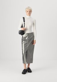 Hvit langermet turtleneck genser, metallisk sølv midi-skjørt med frontsplitt, og svarte sko. Modellen bærer en svart skulderveske.