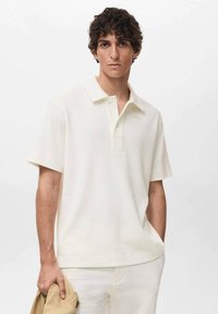 Polo de manga corta en color blanco sucio, hecho de tejido acanalado. Presenta un clásico collar y una tapeta con dos botones.