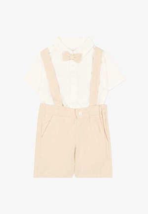 Camicia bianca a maniche corte con colletto e papillon beige, abbinata a pantaloncini beige con bretelle e tasche laterali.