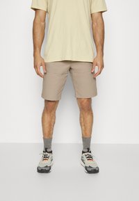 Shorts beiges avec poches, associés à un t-shirt jaune clair. Les chaussures sont des baskets grises et noires avec des accents orange et blancs.