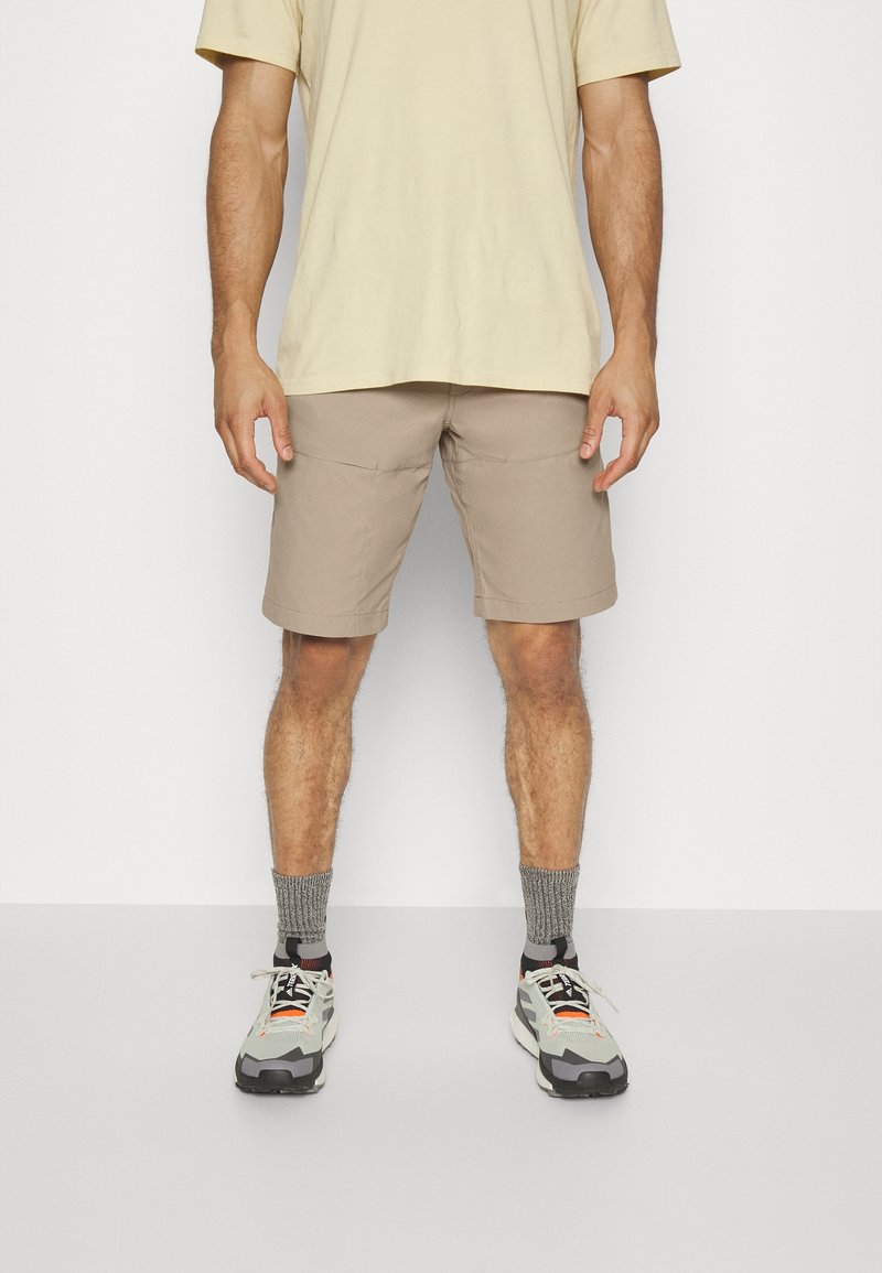 Shorts beiges avec poches, associés à un t-shirt jaune clair. Les chaussures sont des baskets grises et noires avec des accents orange et blancs.