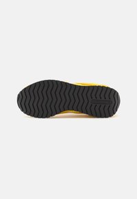 Fekete gumi talp, zigzag mintázattal, élénk sárga felsőrésszel és Reebok márkajelzéssel az oldalon.