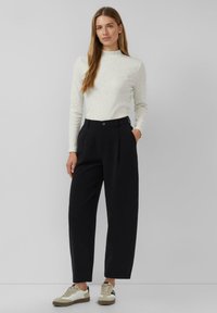 Lichtgrijs, gestructureerd top met lange mouwen en een hoge kraag, gecombineerd met zwart, hooggetailleerd broek en witte sneakers met tan accenten.