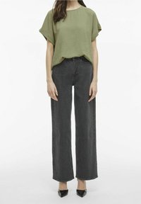 Top verde oliva con trama e maniche corte abbinato a jeans neri a vita alta e gamba larga. La modella indossa tacchi neri con punta a punta.