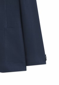 Manche de blazer bleu marine et partie inférieure avant montrant une poche plaquée et un poignet boutonné sur fond blanc.