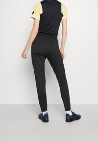Schwarze Sporthose mit tailliertem Design und elastischem Bund. Verfügt über Reißverschlussakzente an den Knöcheln und eine glatte Textur.