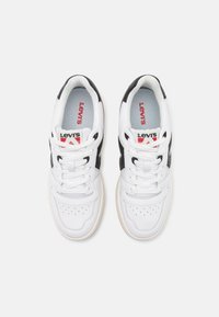 Hvide Levi's sneakers med sorte accenter, perforeret tåboks og flade snørebånd. Sort og rød logo på tungen. Gummisål med let tekstur.