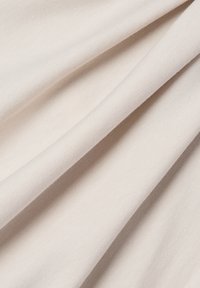 Jasnobeżowa tkanina o gładkiej fakturze, z delikatnym żebrowaniem i łagodnymi fałdami, prezentująca miękki i swobodny design.