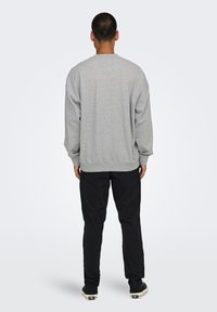 Gray cotton sweatshirt with a crew neck, dropped shoulders, and ribbed cuffs, paired with black pants and casual shoes, viewed from the back.