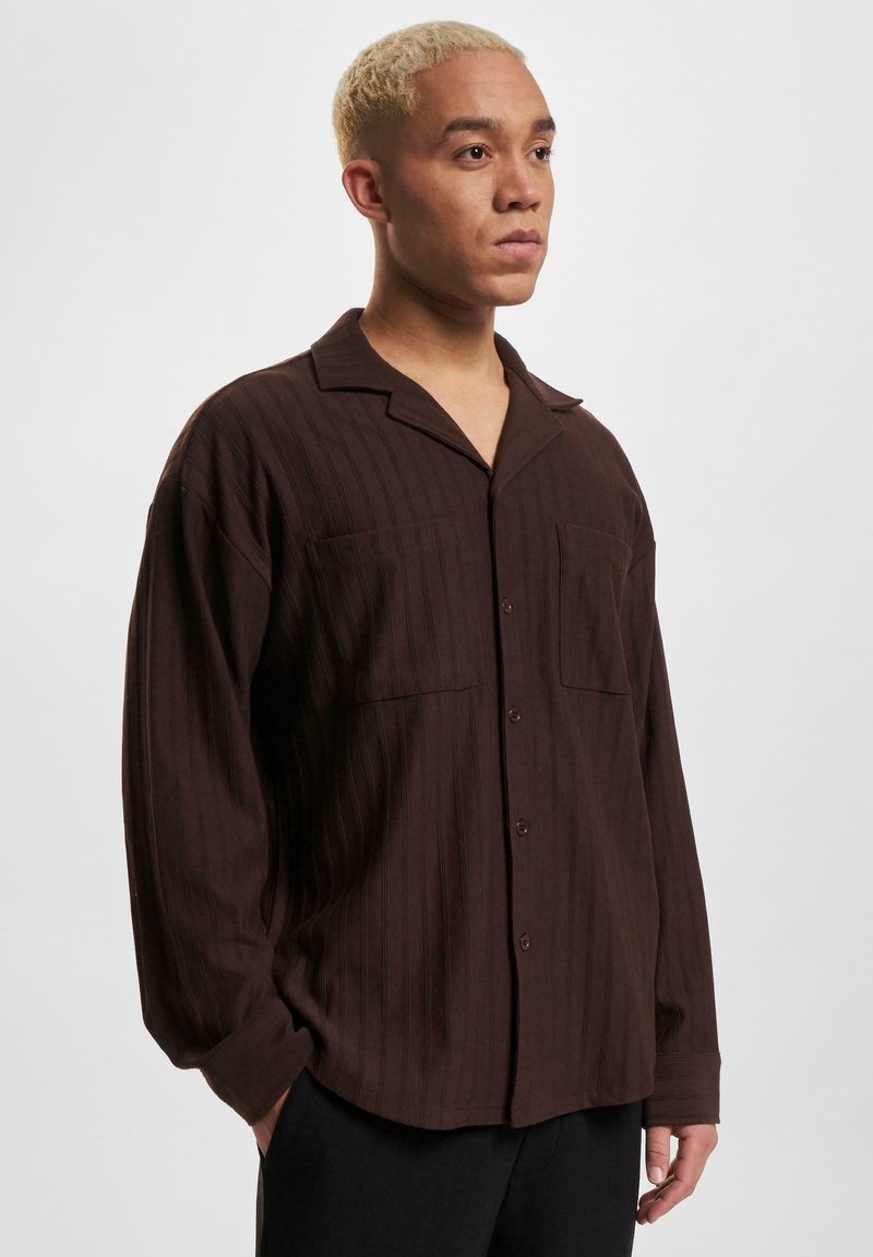Chemise à manches longues rayée marron avec un col à revers, deux poches poitrine, fermeture à boutons et une coupe décontractée, fabriquée à partir d'un tissu texturé.