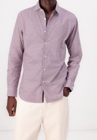 Checkered button-up shirt in burgundy and white, cotton fabric, long sleeves, collar, single chest pocket, straight hem, paired with light trousers.