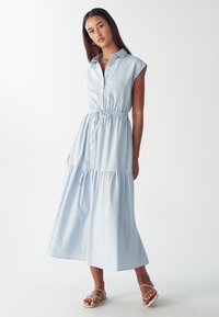 Abito maxi senza maniche di color blu chiaro, con bottoni sul davanti, vita arricciata e gonna a strati. Realizzato in tessuto morbido, presenta una vestibilità comoda.
