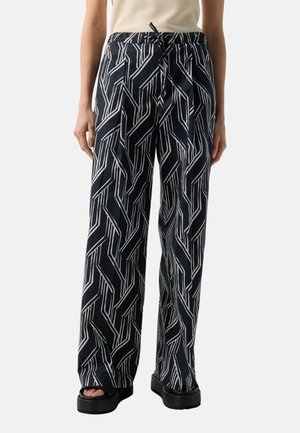 Løse sorte bukser med hvide geometriske linjer, snøre i taljen, forlommer, båret med sorte platformsandaler og en beige top.