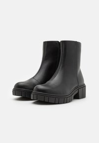 Bottes noires en cuir à cheville avec une semelle épaisse, fermeture éclair sur le côté et un talon en caoutchouc texturé. Finition lisse et design épuré.