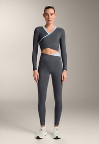 Top grigio a maniche lunghe corto con accenti azzurri, abbinato a leggings grigi a vita alta; realizzato in tessuto elastico, con texture liscia.