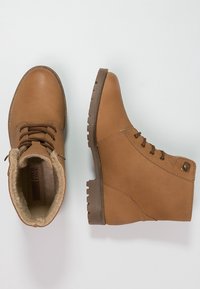 Bottines beige en cuir lisse, avec un laçage à l'avant, doublure en fausse fourrure et semelle en caoutchouc texturée avec un bout arrondi.