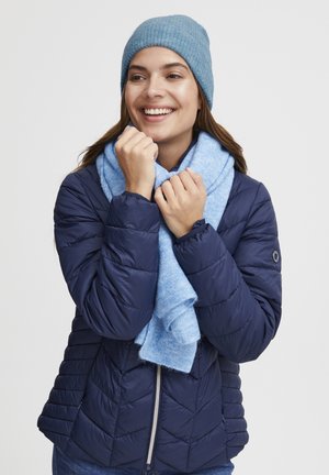 Giacca puffy blu navy con texture trapuntata, accompagnata da una sciarpa azzurro chiaro e un berretto abbinato, il tutto su uno sfondo bianco semplice.