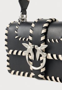 Crna kožna torba s bijelim šavovima, srebrnim prstenom kao naglaskom i dva motiva ptica sprijeda. Kompaktni pravokutni dizajn.