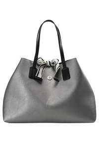 Grand sac cabas argenté avec des poignées noires et un nœud rayé noir et blanc attaché à la base des poignées.